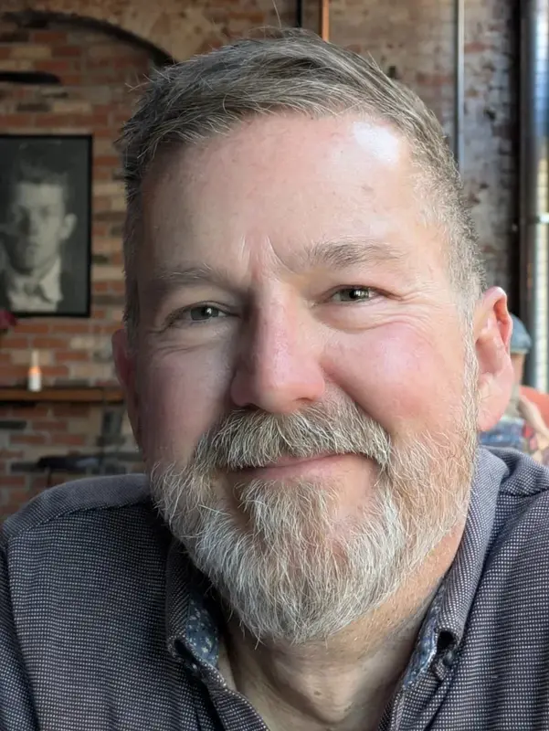 Headshot portrait of Adam Grary smiling with a beard in a casual setting.
