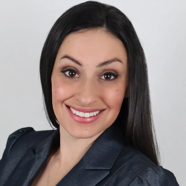 Professional headshot portrait of a smiling businesswoman with dark hair wearing a dark blazer.